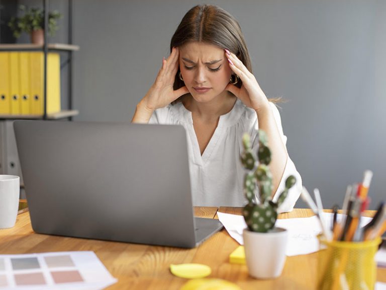 woman at her computer rubbing her temples to relieve headache